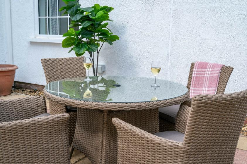 Outdoor wicker and glass table with wine glasses on top.